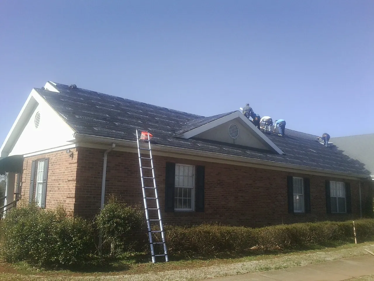 Crew tearing shingles off a brick ranch roof with a ladder set — Metal Roof Repair work by our crew in Danielsville