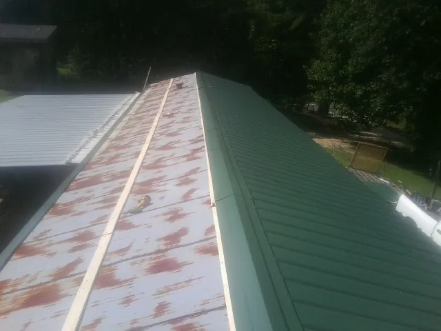 Old rusted panels beside newly installed green metal roofing — Wind Damage Roof Repair by Roofing Brothers in Danielsville