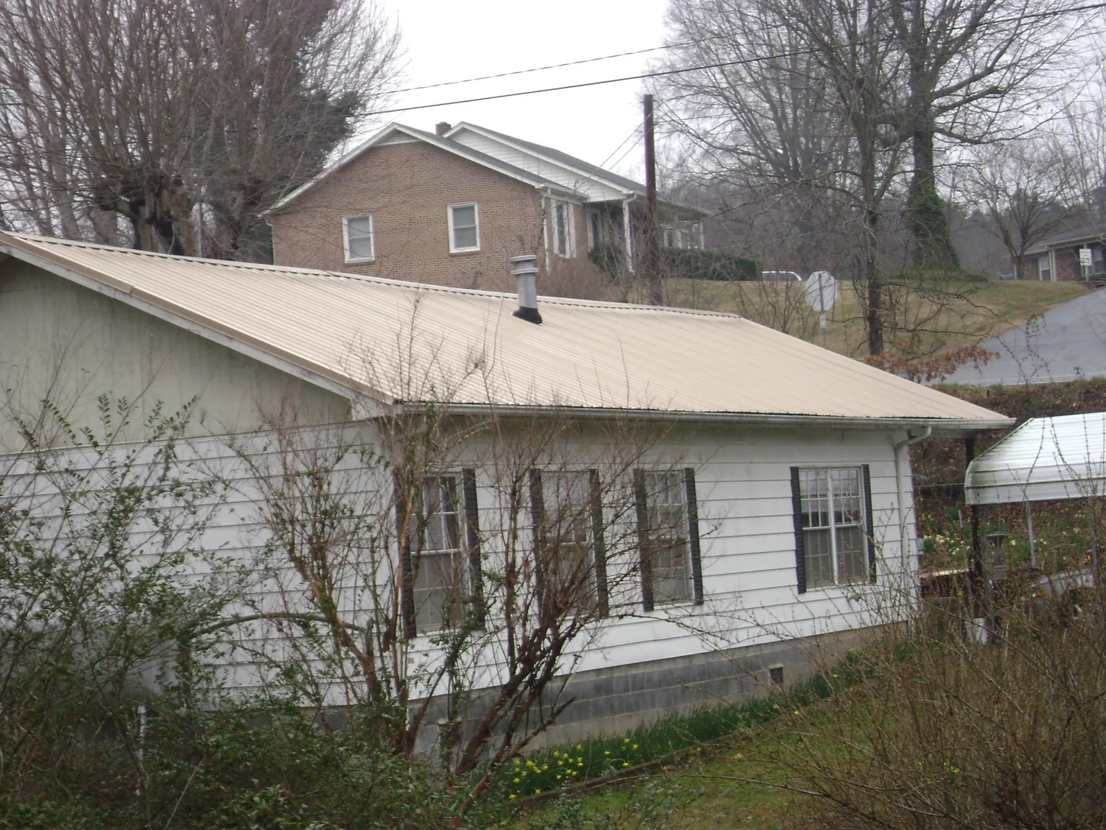 Tan metal roof on a white sided house set into a hillside — Commercial Roofing by Roofing Brothers in Danielsville